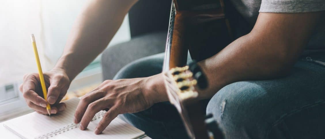 Personne qui tient une guitare et écrit dans un carnet